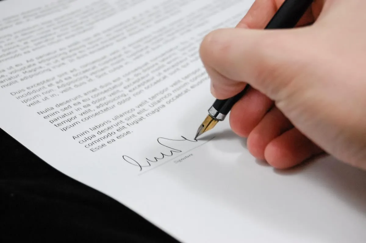 Eine Hand unterschreibt mit einem Füllfederhalter ein Dokument auf der Unterschriftslinie neben dem Wort „Signature“